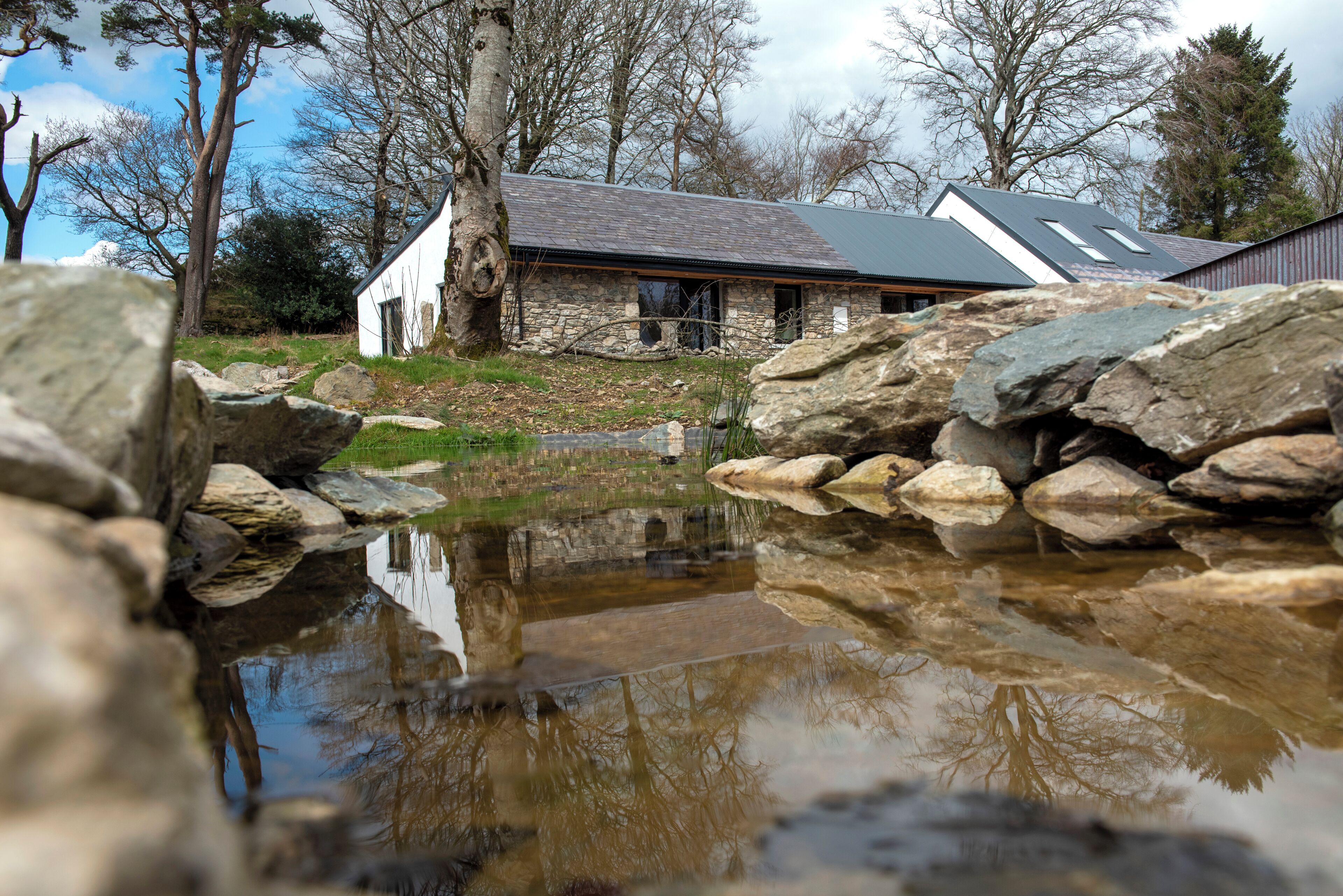 A stone building with a pond in front, surrounded by rocks and trees.