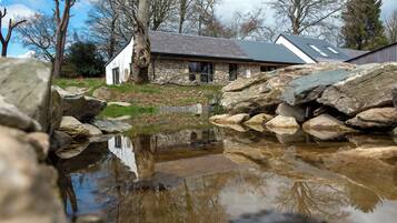 A stone building with a pond in front, surrounded by rocks and trees.