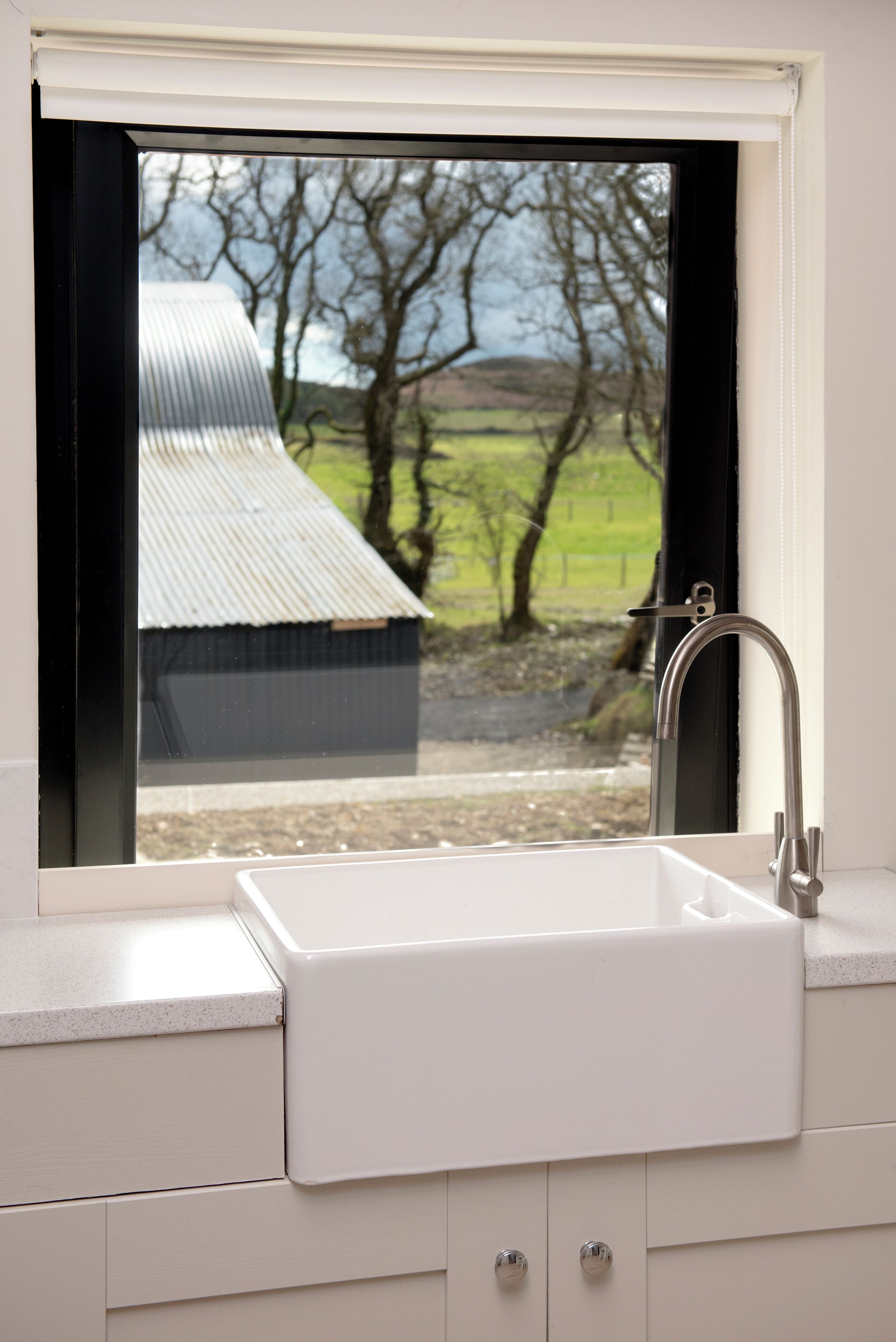 Une salle de bain avec un lavabo blanc, un robinet et une fenêtre donnant sur une maison et des arbres.