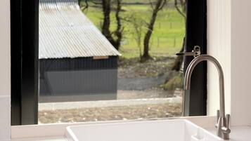 Une salle de bain avec un lavabo blanc, un robinet et une fenêtre donnant sur une maison et des arbres.