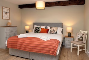 A bedroom with a bed, two bedside tables, a chair, a dresser, and a wall with a framed picture.