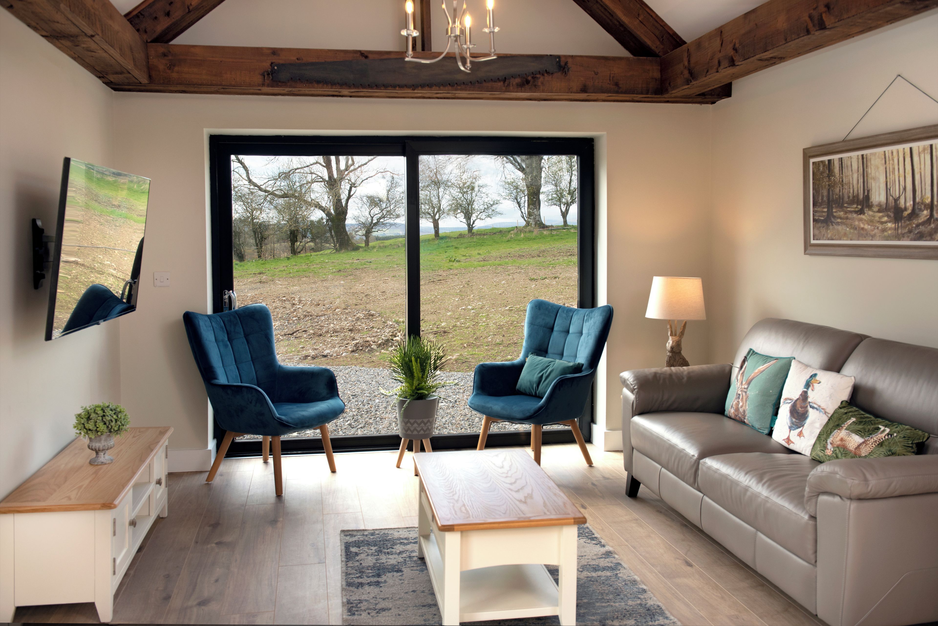 A living room with a large window, two blue chairs, a sofa, a coffee table, and a painting on the wall.