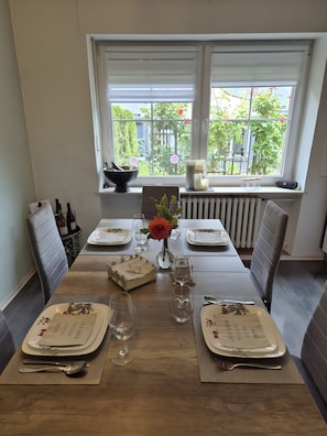 A dining table set for four with a vase of flowers, a bowl, candles, and a window view. - Guesthouse 'Eifelglück' with Private Terrace, Garden, and Wi-Fi (Großlittgen)