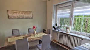 A dining area with a table, chairs, a vase with a flower, and a window with a view of greenery. - Guesthouse 'Eifelglück' with Private Terrace, Garden, and Wi-Fi (Großlittgen)