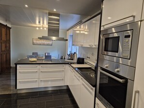 A modern kitchen with stainless steel appliances, white cabinetry, and a black countertop. - Guesthouse 'Eifelglück' with Private Terrace, Garden, and Wi-Fi (Großlittgen)