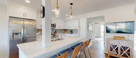 A modern kitchen with a central island, stainless steel appliances, and a dining area with wicker chairs.