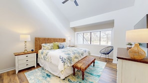 A bedroom with a large bed, bedside tables, a bench, a chair, a window with blinds, and a ceiling fan. - Beautiful Three Bedroom Villa with Sweeping Views of George Fazio Golf Course (Hilton Head)