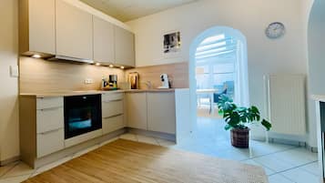 A modern kitchen with a built-in oven, white cabinets, and a wooden floor. There is a potted plant and a clock on the wall.