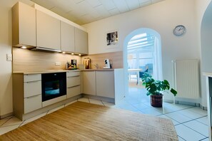 Eine moderne Küche mit Einbauofen, weißen Schränken und Holzboden. An der Wand befinden sich ein Topf mit Pflanze und eine Uhr.