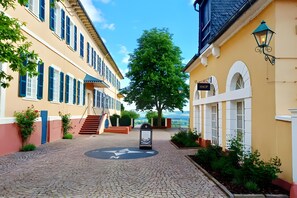 A cobblestone street with buildings on either side, a tree in the center, and a sign indicating a shop.