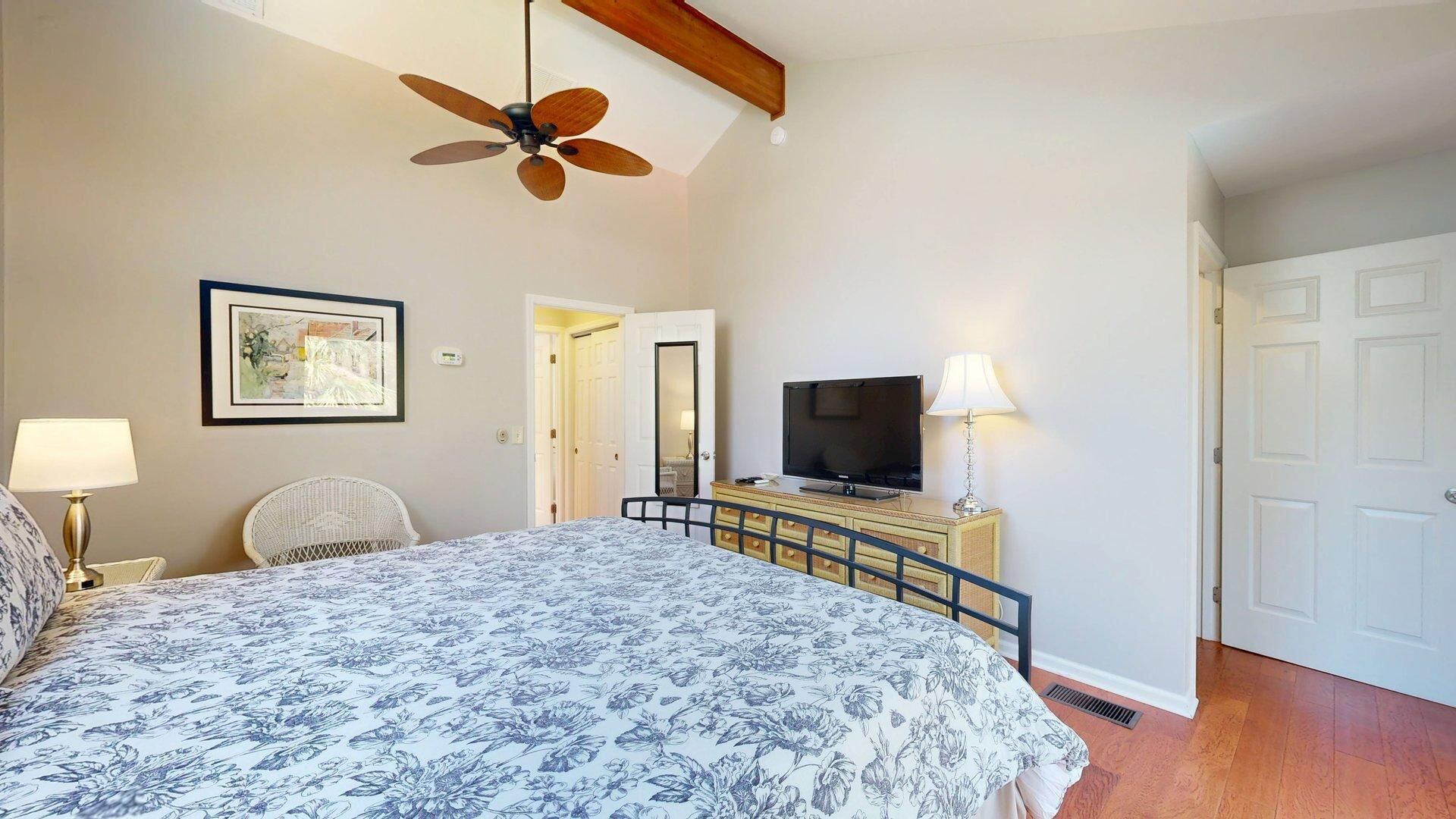 A bedroom with a bed, a ceiling fan, a television, a dresser, and a door.