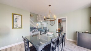 A modern dining area with a glass table and chairs, a chandelier, and a clock on the wall. - 4 Bedroom 4 Bath house on the 11 mile lagoon (Hilton Head)