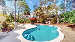 Une piscine à bords incurvés, entourée de chaises longues et d’une table à manger avec un parasol.