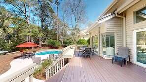 Une terrasse avec une piscine, du mobilier d’extérieur et une vue sur les arbres environnants.