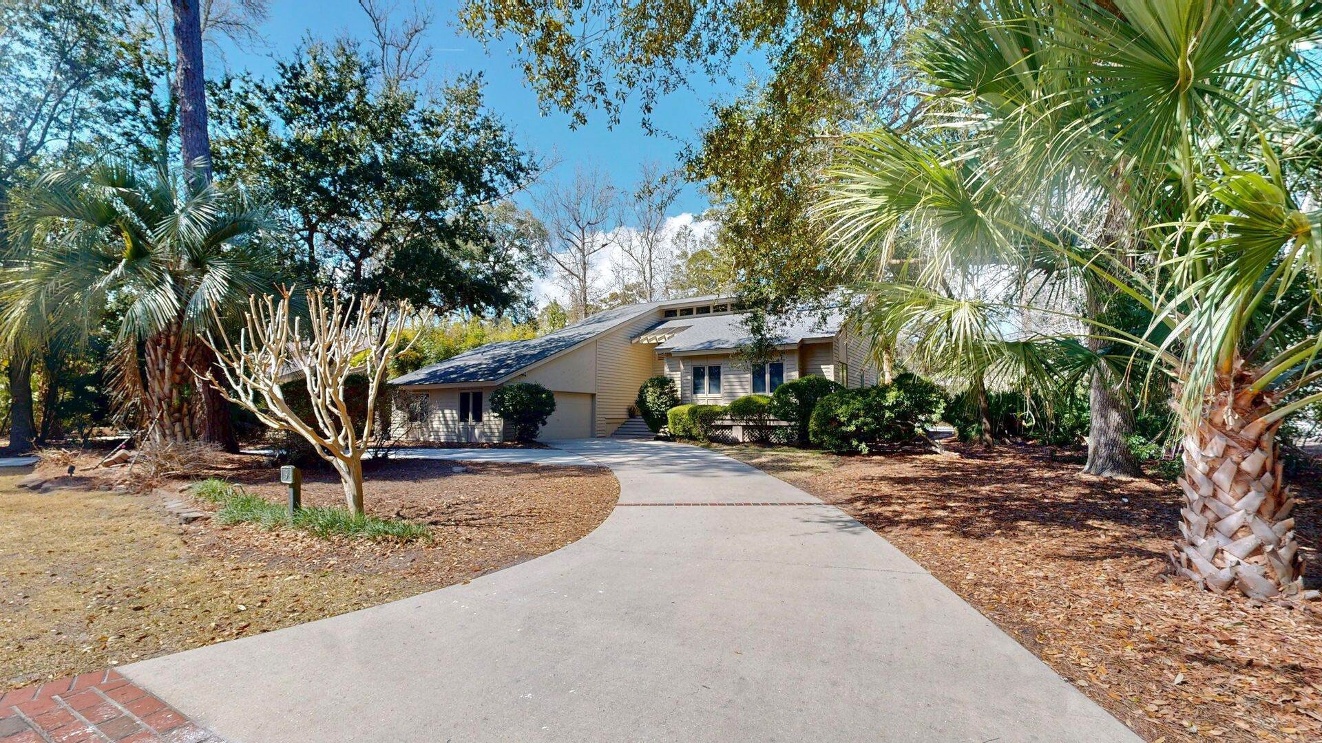 A residential property with a paved driveway leading to a house, surrounded by mature trees and a well-maintained lawn.