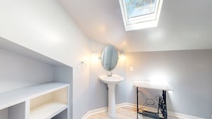 Un baño con tragaluz, lavamanos pedestal y tocador con estantes abiertos.