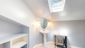 Ein Badezimmer mit Dachfenster, einem Standwaschbecken und einem Waschtisch mit offenen Regalen.