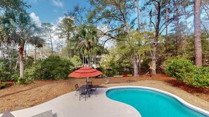 A swimming pool with a patio area, surrounded by trees and a red umbrella. - 4 Bedroom 4 Bath house on the 11 mile lagoon (Hilton Head)