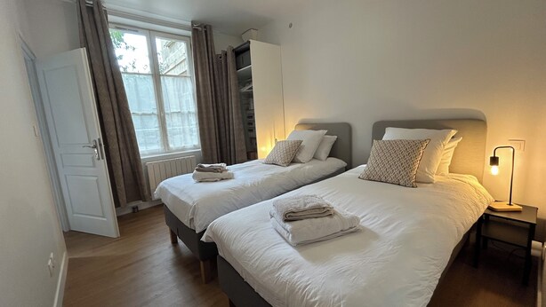 A bedroom with two beds, a wardrobe, a window with curtains, and a bedside lamp. - LE REFUGE DU MOULIN - 2-Bedroom Apartment in Downtown Senlis (Parking) (Senlis)