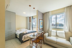 Een hotelkamer met een bed, een bank, een eettafel en een raam met gordijnen.