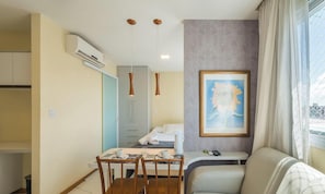 Een hotelkamer met een bed, een eettafel met stoelen, een bank, een schilderij aan de muur en een airconditioner.