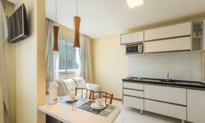 Een moderne keuken met witte kasten, een magnetron en een eethoek met een tafel voor twee personen.