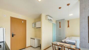 Ein Hotelzimmer mit Holztür, einer kleinen Küchenzeile, einem Essbereich mit Tisch und Stühlen sowie einem Bett mit weißer Daunendecke.