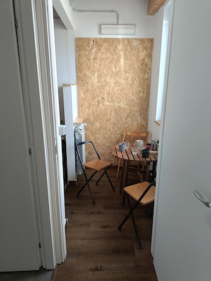 A room with a wooden floor, a table with chairs, a radiator, and a wall with a textured surface.