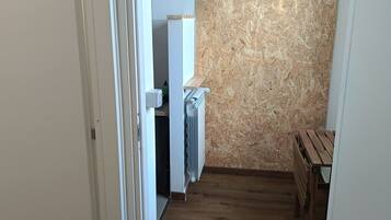 Ein schmaler Flur mit Holzboden, eine weiße Tür links und ein Küchenbereich mit einer Holzverkleidung und einem Heizkörper rechts.