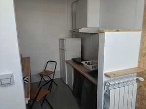 A compact kitchen with a refrigerator, a sink, and a chair.