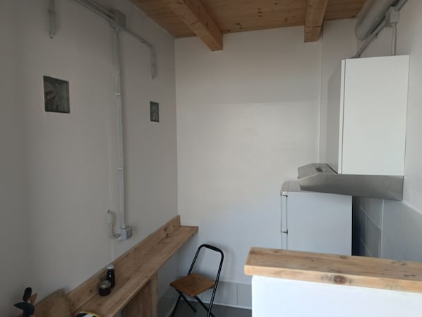 A small, compact kitchen with a wooden bench, a chair, and a white cabinet.