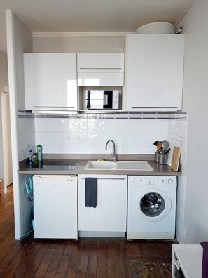 Een compacte keuken met een ingebouwde magnetron, een spoelbak en een wasmachine.