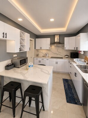 A modern kitchen with white cabinetry, a central island with stools, a stainless steel microwave, and a built-in stove.