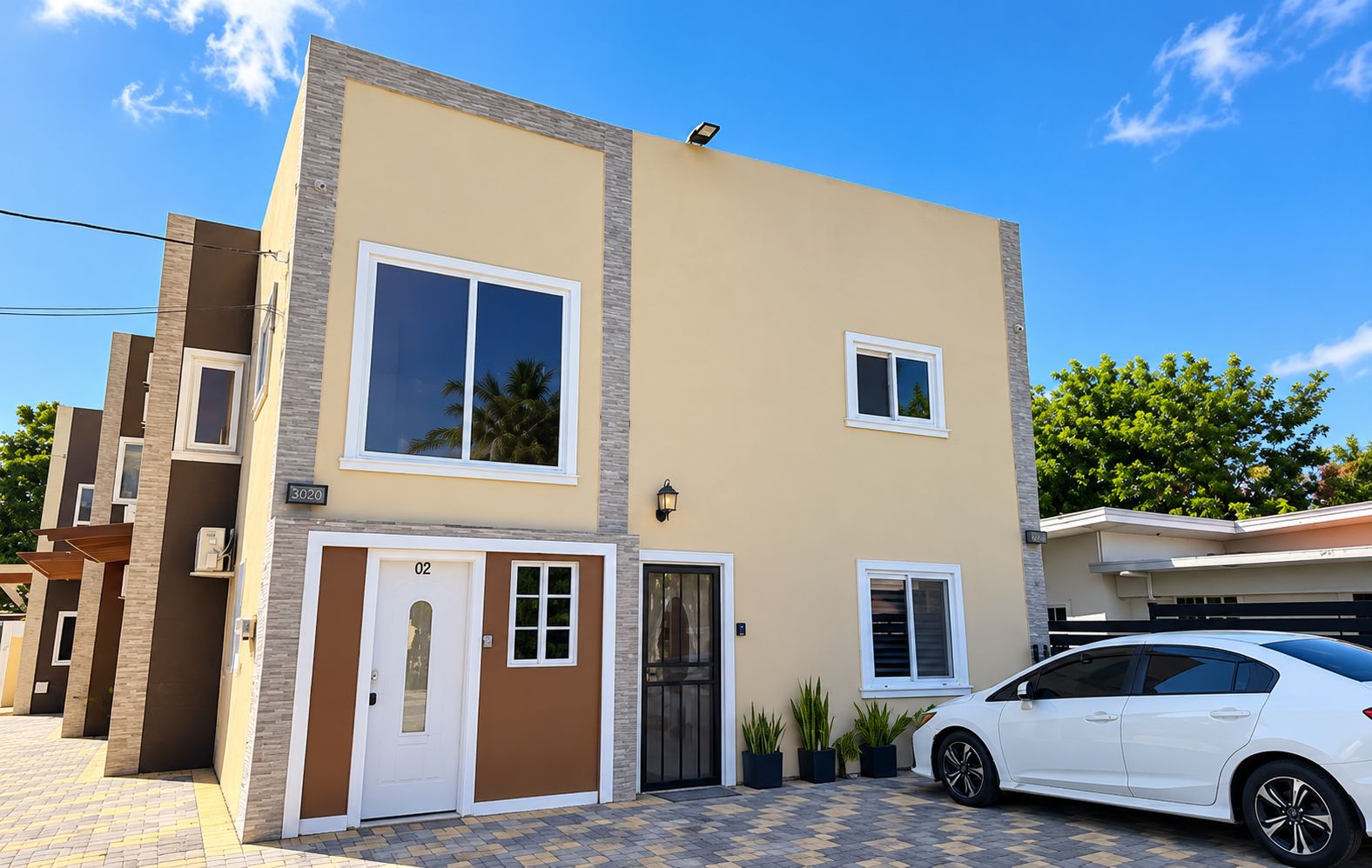 Un immeuble résidentiel de deux étages, doté d’une façade beige, d’une porte blanche et d’une voiture blanche garée dans l’allée.