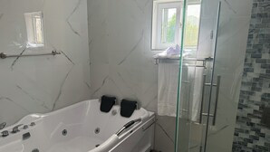 Um banheiro moderno com parede de mármore, chuveiro com box de vidro e banheira branca com assentos de banho pretos.
