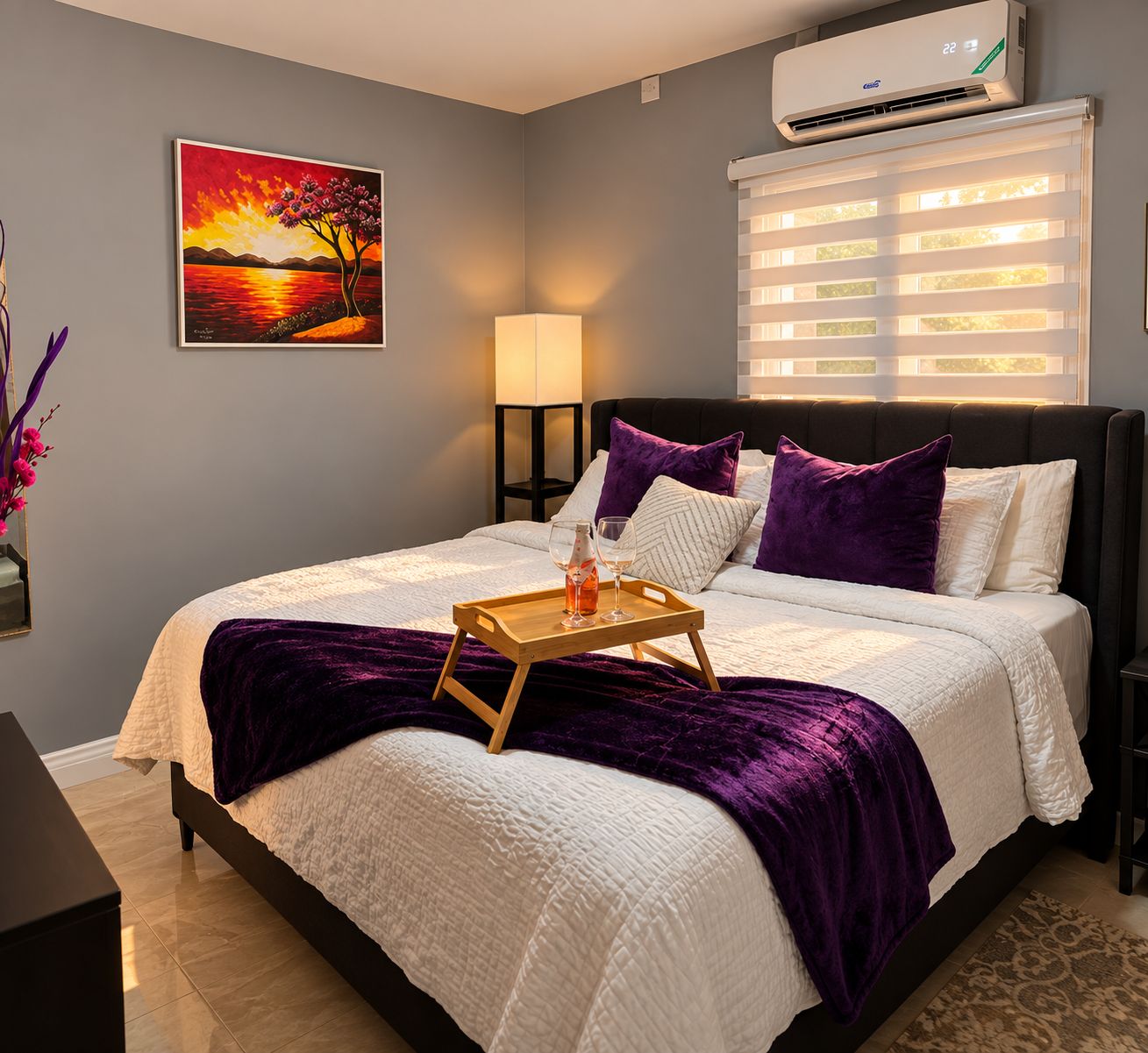 A bedroom with a bed, a bedside table, a lamp, a painting, an air conditioner, and a window with blinds.