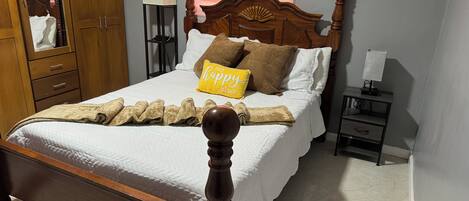 Un lit bien fait, avec un oreiller sur lequel est écrit « mon endroit préféré », une lampe de chevet et une armoire en bois.