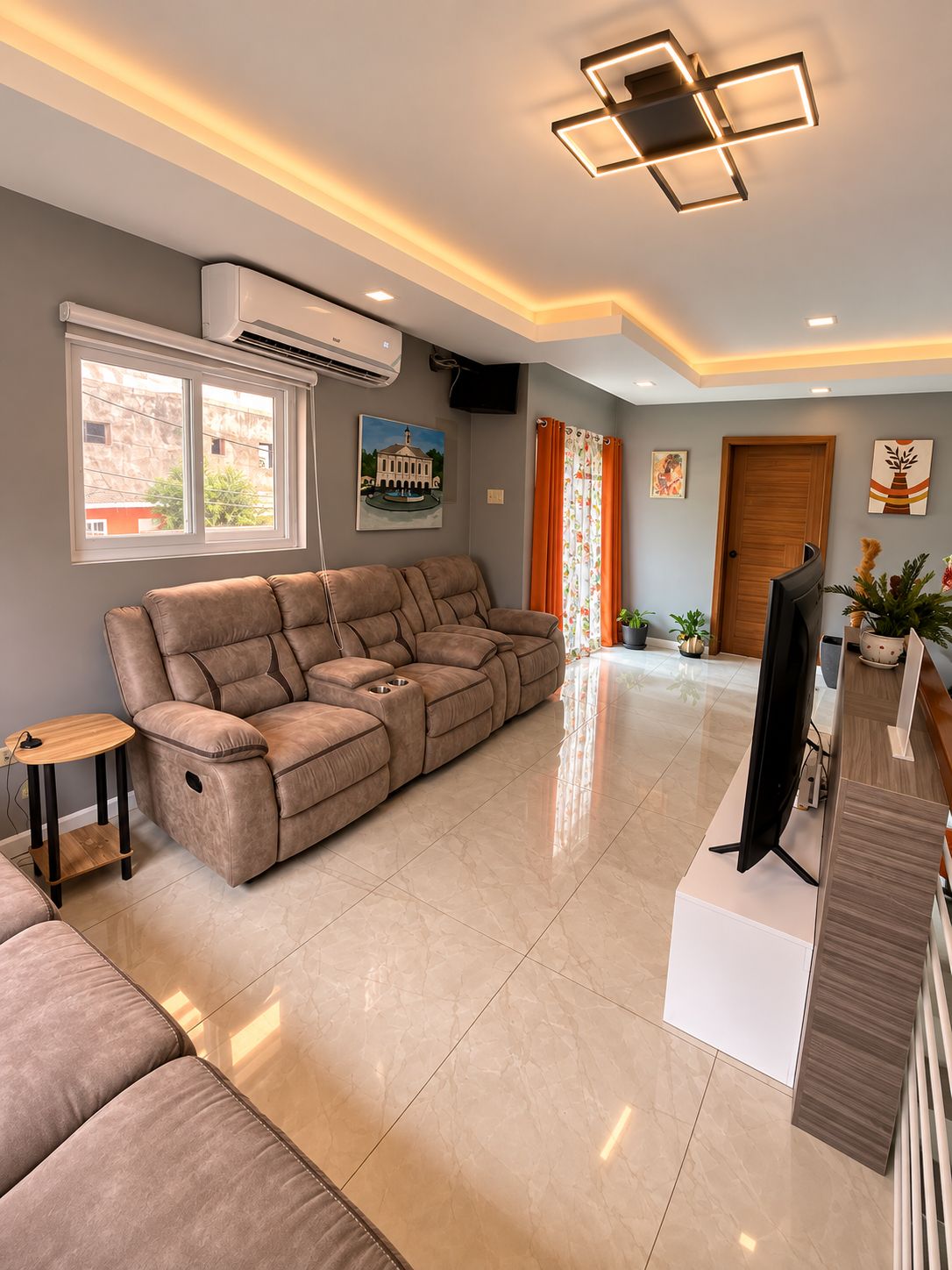 A modern living room with a sectional sofa, a flat-screen TV, and a ceiling light fixture.