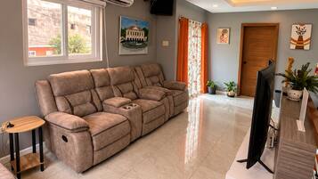 A modern living room with a sectional sofa, a flat-screen TV, and a ceiling light fixture.