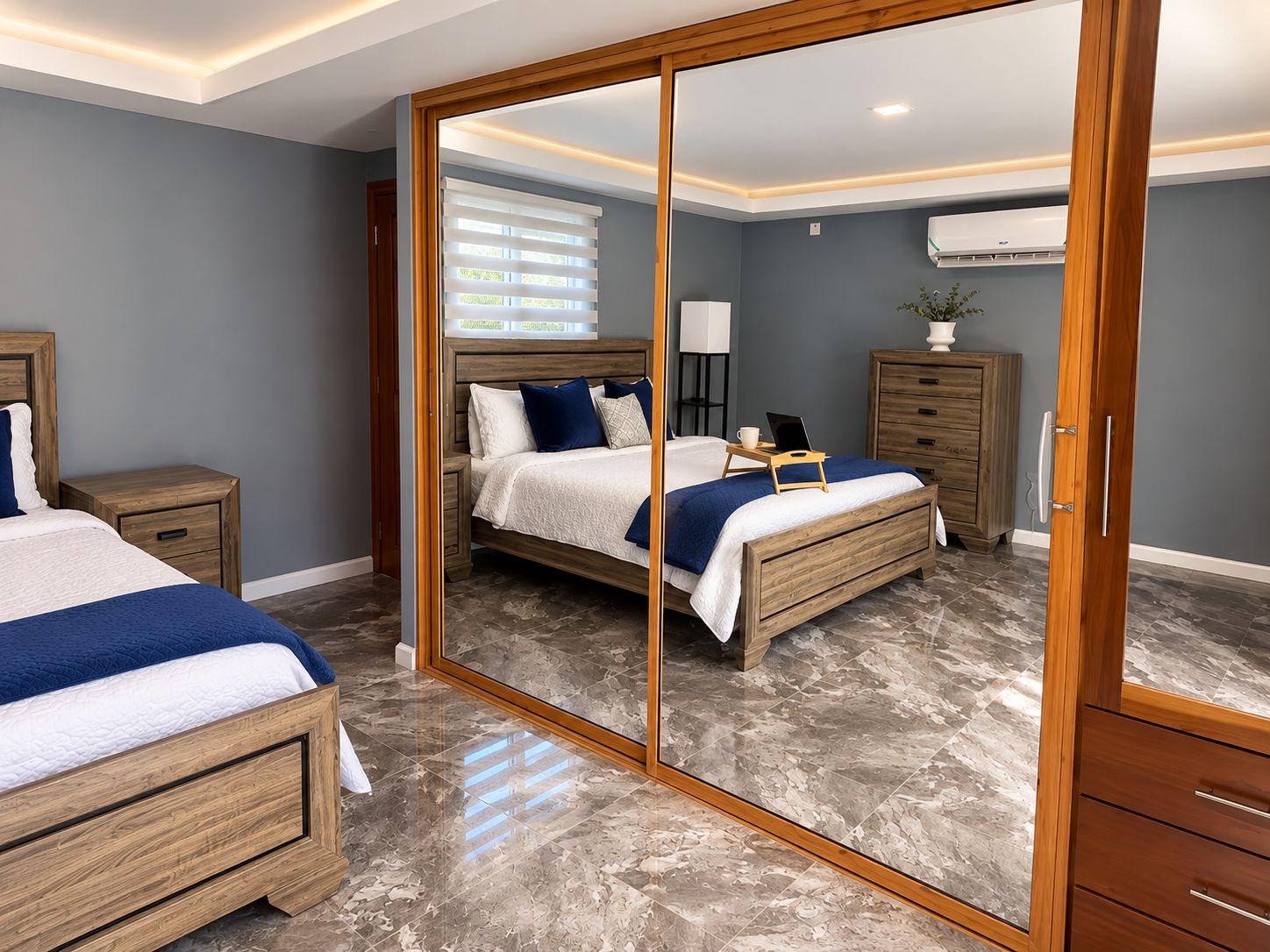 A bedroom with a large mirror, a bed, bedside tables, a dresser, and an air conditioning unit.
