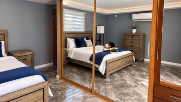 A bedroom with a large mirror, a bed, bedside tables, a dresser, and an air conditioning unit.