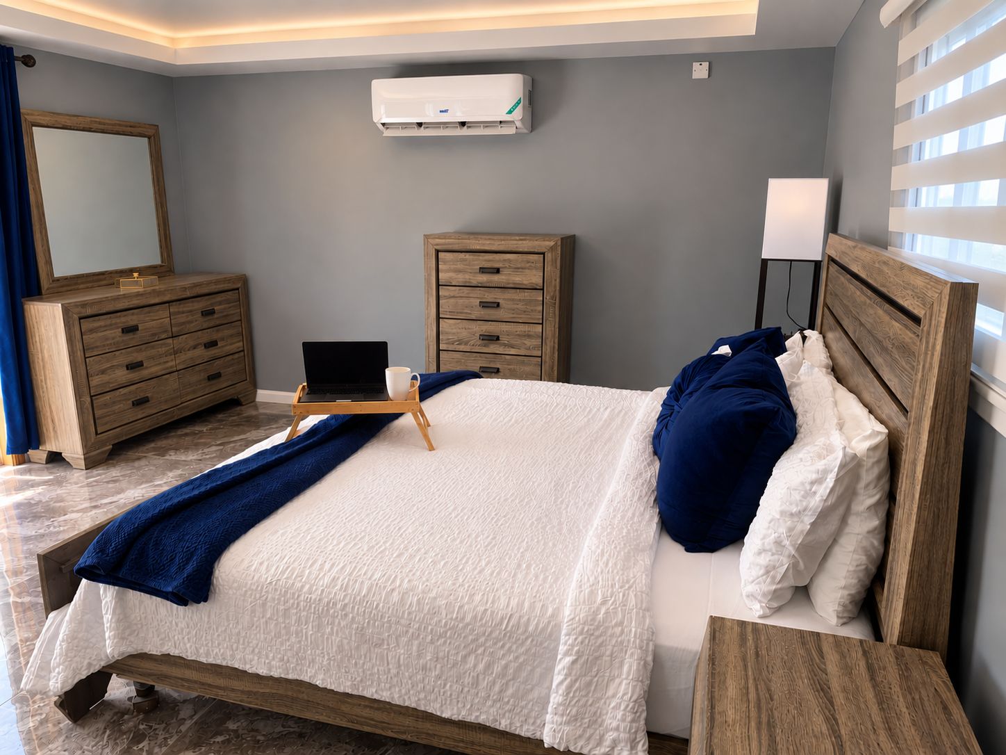 A bedroom with a bed, bedside tables, a dresser, a mirror, and an air conditioning unit.