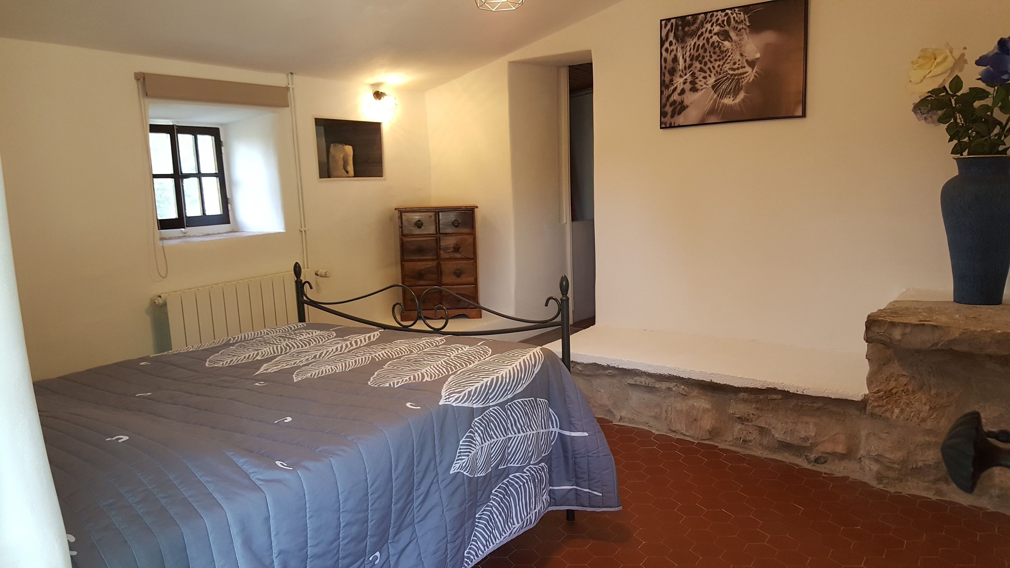 Ein Schlafzimmer mit einem Bett, einem Schminktisch, einem Fenster, einer Wandleuchte und einem Gemälde.