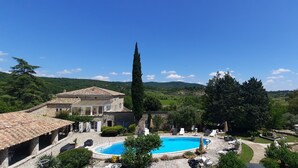 Un’area piscina con edifici in pietra, un alto cipresso e vista su dolci colline.