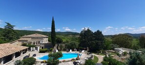 Ein Poolbereich mit Steingebäuden, einer hohen Zypresse und Blick auf sanfte Hügel.