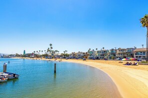 A beach with a clear blue sky, a sandy shore, and a row of buildings in the background. - Baby Beach 2BR, Walk to Everything W/Parking & AC! (Newport Beach)