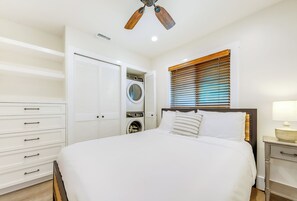 Un dormitorio con una cama, ventilador de techo, lavadora y ventana con persianas.