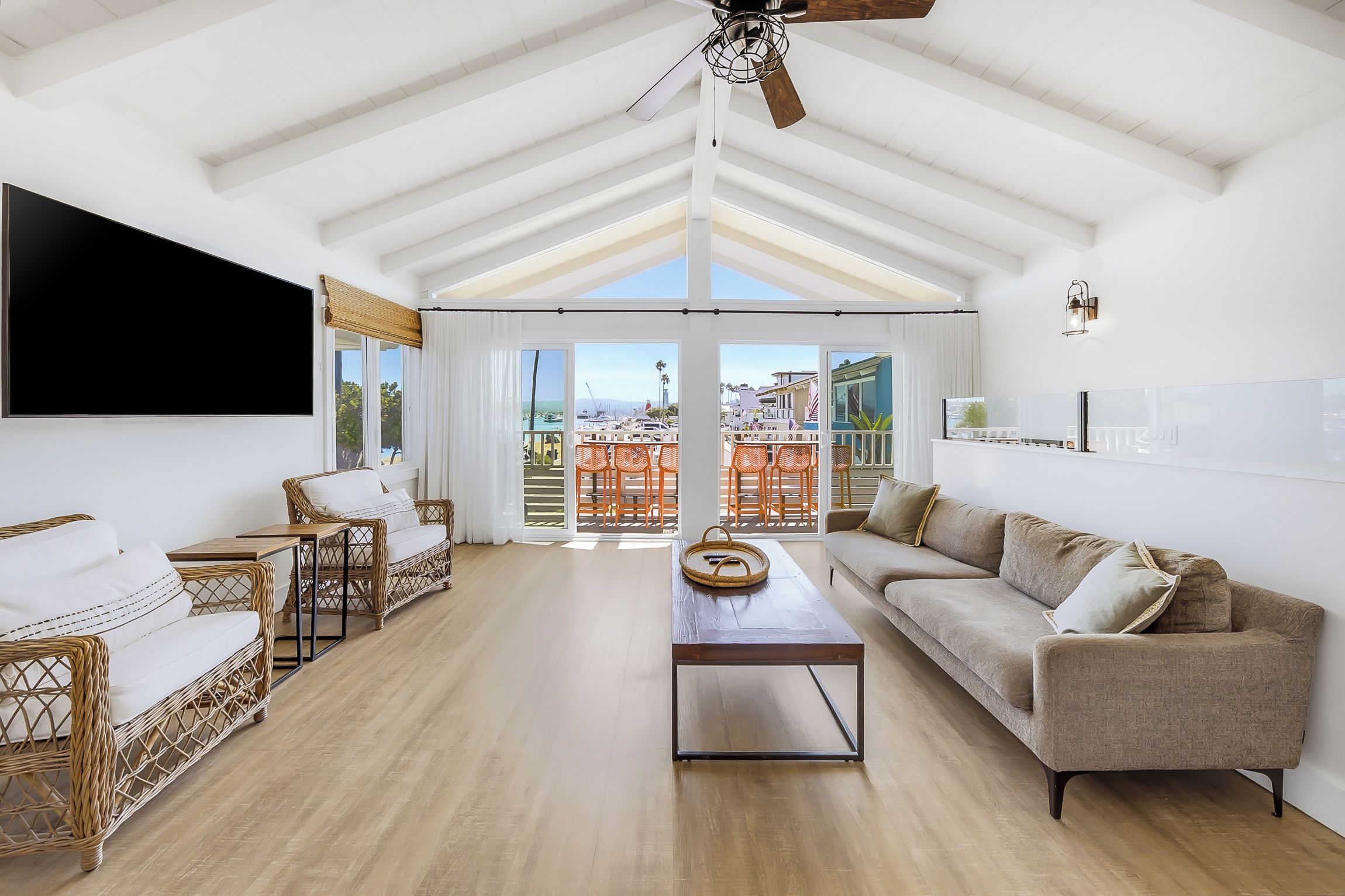 A spacious living room with a high ceiling, a ceiling fan, and a large window overlooking a balcony with outdoor furniture.