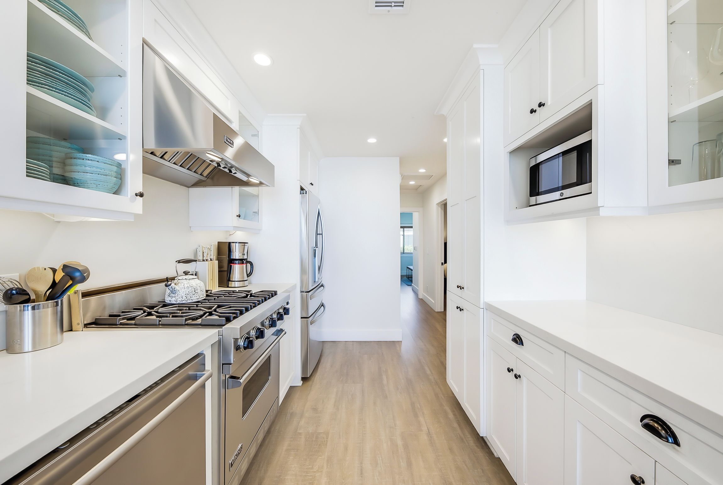 A modern kitchen with white cabinetry, stainless steel appliances, and a wooden floor.