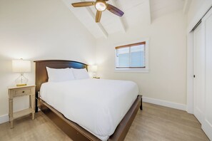 Ein Schlafzimmer mit einem Bett, Nachttischen, einem Deckenventilator, einem Fenster mit Jalousien und einer Tür.